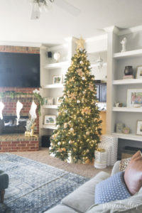 Modern Glam Christmas tree with gold ornaments, brass tree collar, glittered magnolia leaves and white and gold Christmas gifts add the perfect touch to these custom built-ins.