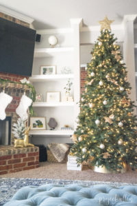 Modern Glam Christmas tree with gold ornaments, brass tree collar, glittered magnolia leaves and white and gold Christmas gifts tadd the perfect touch to these custom built-ins.