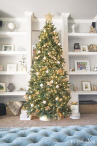 Modern Glam Christmas tree with gold ornaments, brass tree collar, glittered magnolia leaves and white and gold Christmas gifts tadd the perfect touch to these custom built-ins.