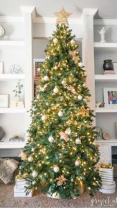Modern Glam Christmas tree with gold ornaments, brass tree collar, glittered magnolia leaves and white and gold Christmas gifts add the perfect touch to these custom built-ins.