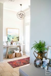 Welcome to our Spring Home Tour: See how we transformed our home with just a few simple changes, console table with framed art canvas. white lamps, vintage rug and decorative baskets under a orb chandelier create an inviting entryway.