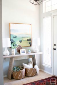 Welcome to our Spring Home Tour: See how we transformed our home with just a few simple changes, console table with framed art canvas. white lamps, vintage rug and decorative baskets under a orb chandelier create an inviting entryway.