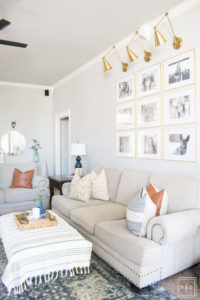 Welcome to our Spring Home Tour: See how we transformed our home with just a few simple changes, a brass frame gallery wall with gold swing arm sconces frame this neutral sofa adorned with mudcloth and leather pillows and black modern ceiling fan,