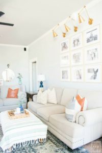 Welcome to our Spring Home Tour: See how we transformed our home with just a few simple changes, a brass frame gallery wall with gold swing arm sconces frame this neutral sofa adorned with mudcloth and leather pillows and black modern ceiling fan,
