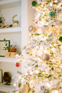 Christmas Decorations, Flocked Christmas tree, white lights, gold bows, white and gold ornaments, white and gold wrapping paper and white gift boxes in front of built-in shelves styled with curated items. Modern Glam Christmas ideas, Christmas decorating ideas. tree collars, ornaments, stockings, wrapping paper, garland and Christmas lights.
