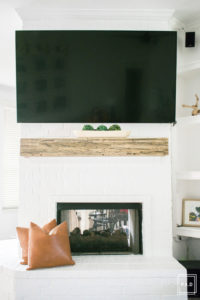 breath of fresh air spring home tour: White painted brick fireplace with reclaimed wood mantel accented with a wood dough bowl and leather pillow